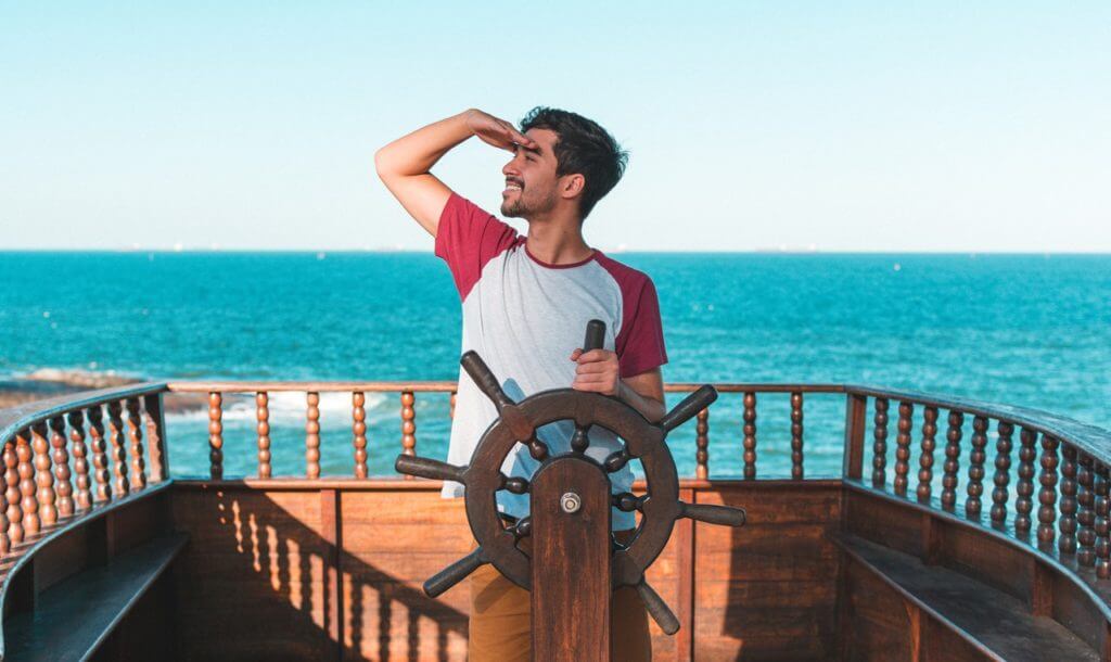 young man mugging at helm of ship