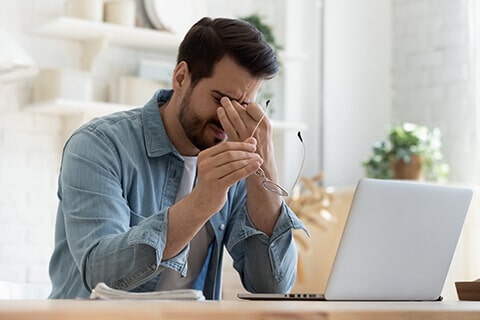 Man rubbing his eyes in front of computer