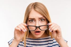 woman looking underneath glasses that she is holding in front of her face
