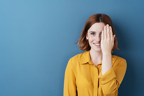 Woman with red hair and yellow shirt covering one eye.