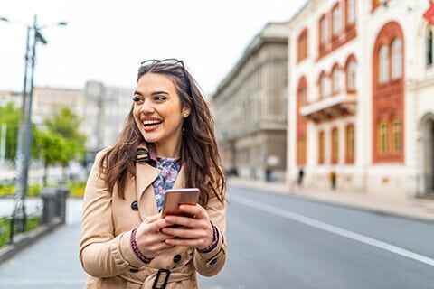 Smiling Woman On Mobile Phone On sidewalk